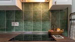 Una cocina con salpicadero de azulejos verdes, una placa de inducción empotrada y una cesta con utensilios de cocina sobre la encimera.