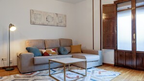 Una sala de estar con un sofá, una mesa de centro, un tapete estampado, una lámpara de pie y una puerta de madera.