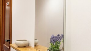 Un pasillo con puerta de madera, pared blanca, estante de madera con dos cuencos y una planta en maceta.