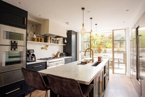 A modern kitchen with stainless steel appliances, a central island, and pendant lighting. - The Luxury Fulham Townhouse (Parsons Green, London, UK)