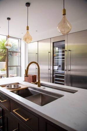 A modern kitchen with a stainless steel sink, pendant lights, and a view of a cityscape through large windows. - The Luxury Fulham Townhouse (Parsons Green, London, UK)
