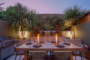 An outdoor dining area with a table set for four, surrounded by chairs, and a grill to the left. - The Luxury Fulham Townhouse (Parsons Green, London, UK)