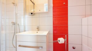 Un baño con cabina de ducha de vidrio, un lavamanos blanco y una pared decorativa roja.
