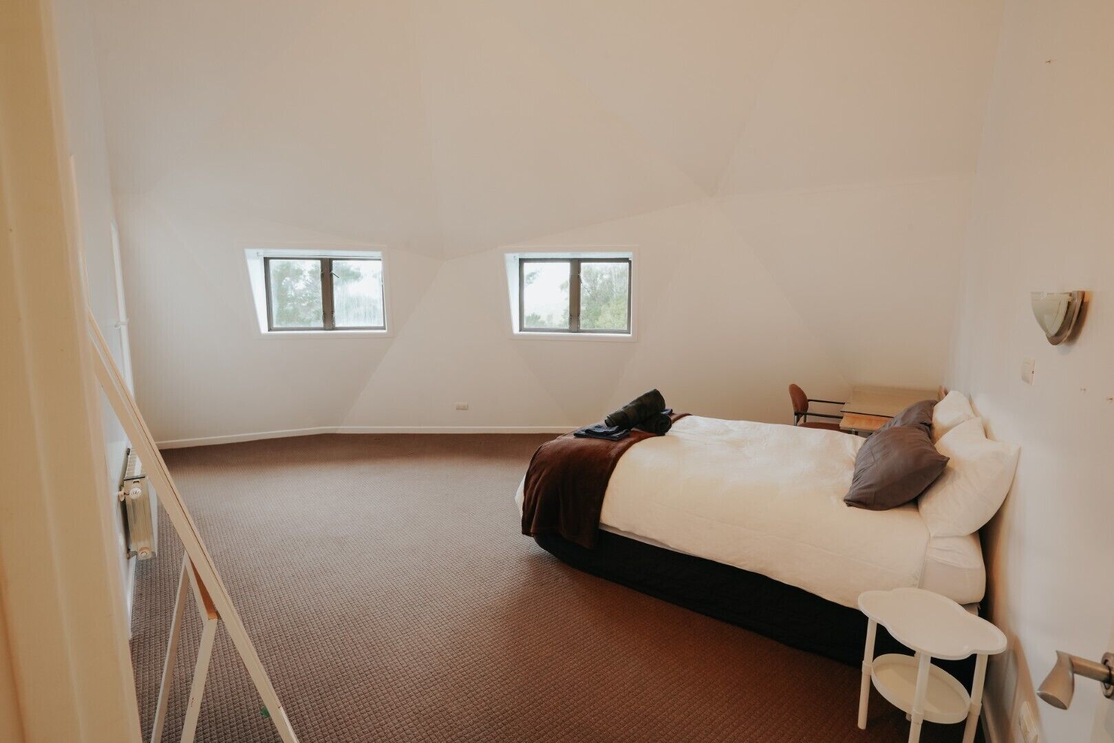 Une chambre à coucher avec un lit, deux fenêtres, une chaise et une petite table.