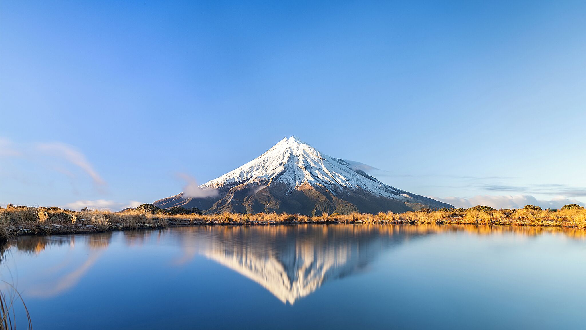 A snow-capped mountain reflected in a calm lake with clear skies.
