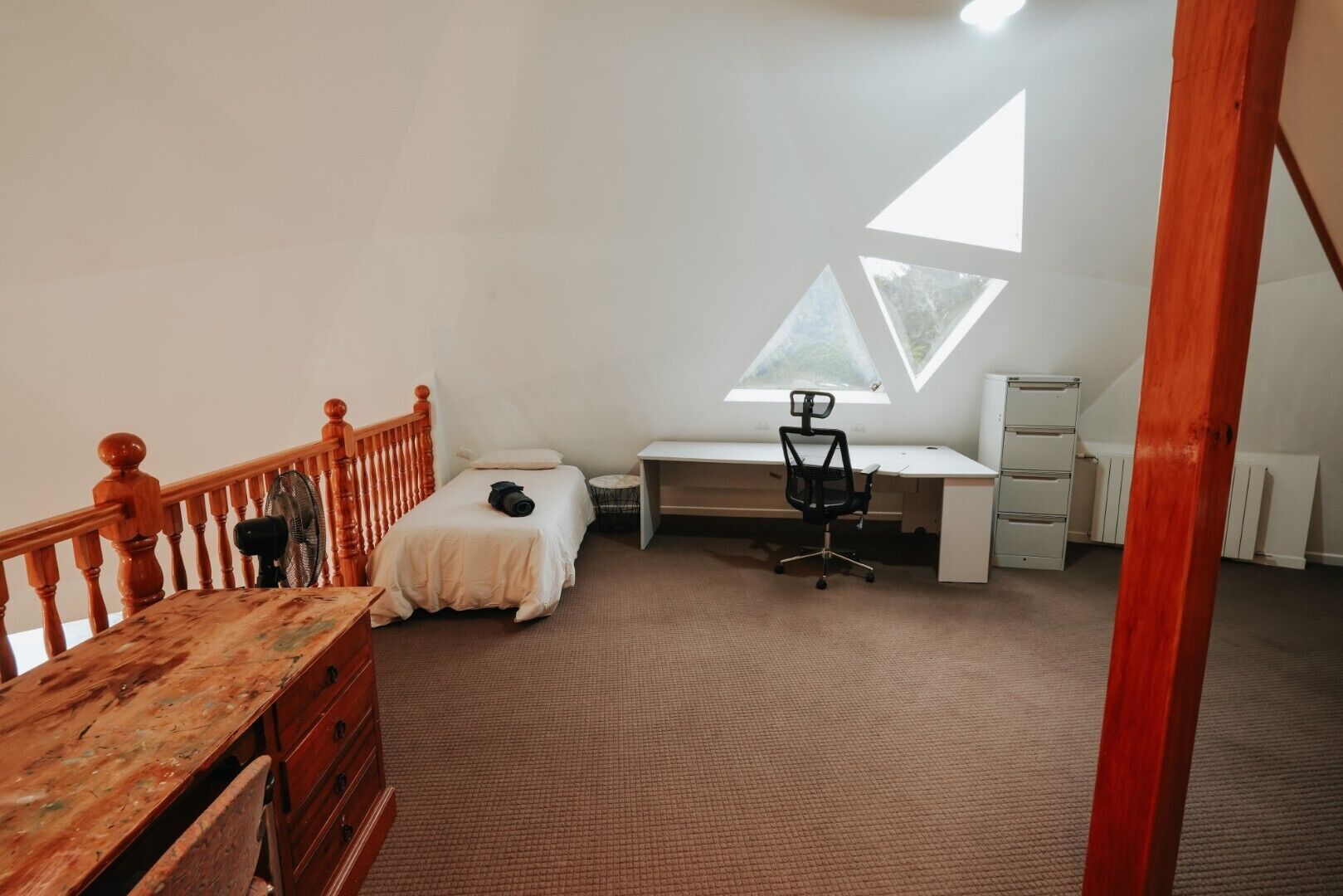 A bedroom with a bed, desk, chair, and a wooden dresser.