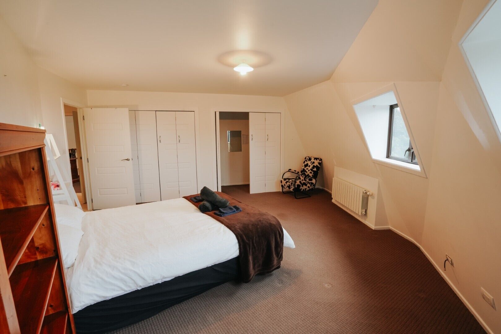 A bedroom with a bed, a wardrobe, a radiator, a window, and a chair.