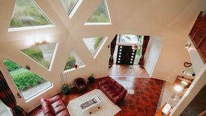 Un loft amplio con ventanas grandes, piso de baldosas rojas, sofá de cuero y una mesa de centro blanca.