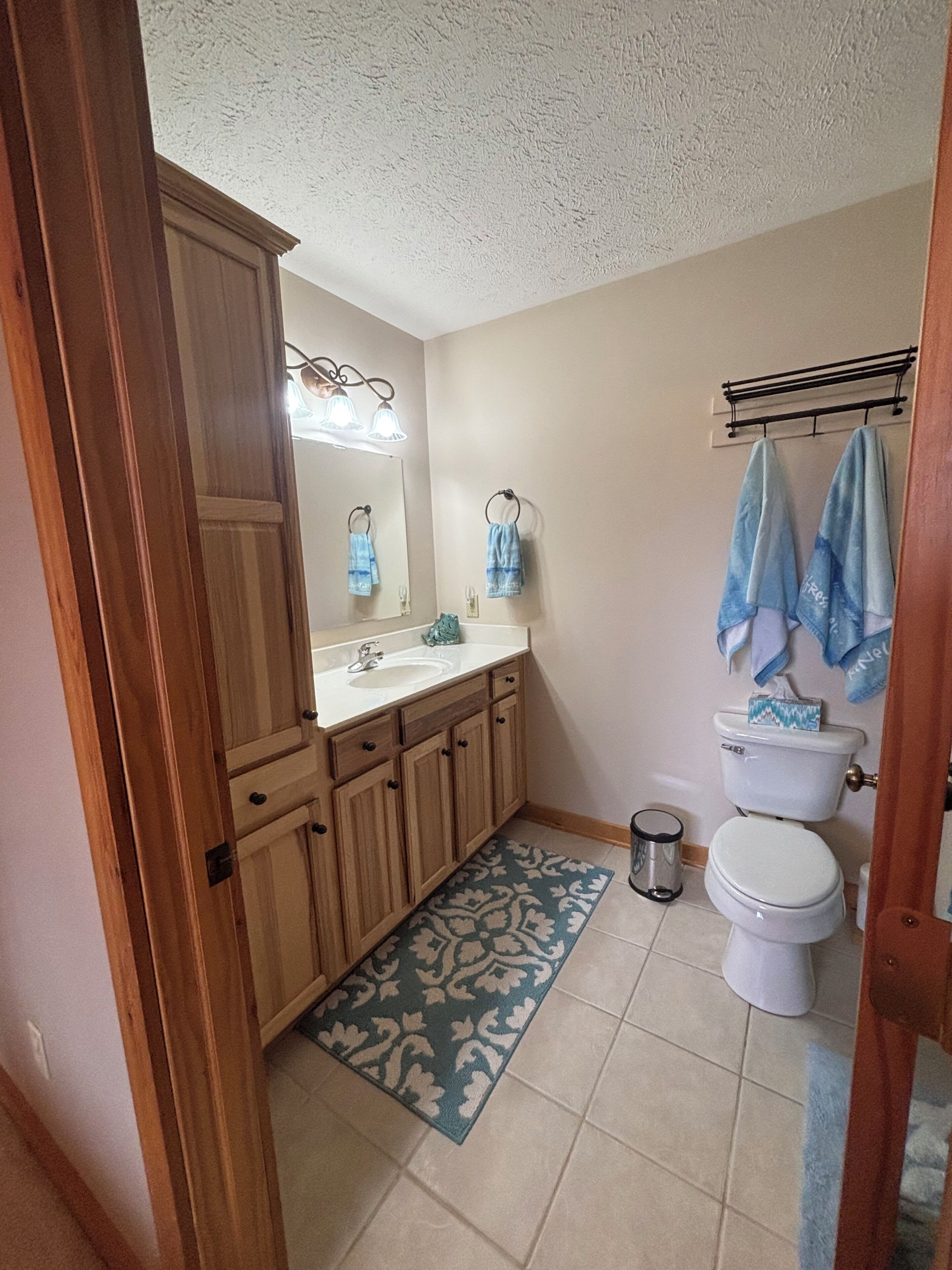 Een badkamer met houten kastjes, een wastafel, een toilet, een spiegel en een blauw tapijt met een patroon.