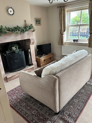 Una sala de estar con sofá, chimenea, televisión y ventana con cortinas.