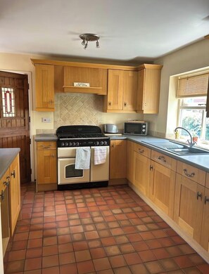 Una cocina con armarios de madera, estufa, microondas y piso de baldosas.