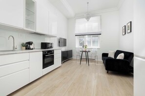 Une cuisine moderne avec des meubles blancs, un coin repas doté d’un canapé noir et un lustre.