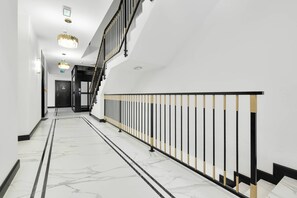 Un couloir doté d’un sol en marbre, d’une rambarde noire et dorée, et d’un escalier avec des balustrades noires.