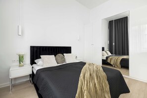Une chambre à coucher moderne avec un grand lit, une table de chevet, un miroir et une lampe fixée au mur.