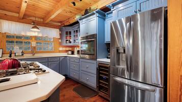 A kitchen with wooden ceiling beams, a stainless steel refrigerator, a built-in oven, and a large island with a red kettle.