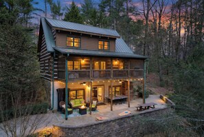 Une cabane en rondins dotée d’un balcon, d’un espace salon extérieur et d’un foyer.