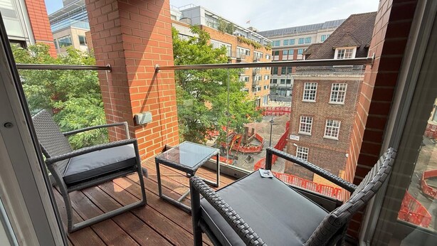 A balcony with wicker furniture, a glass table, and a brick pillar. - Westminster Apartment - Big Ben (London)