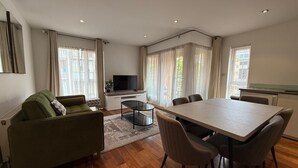A modern living room with a sofa, TV, dining table, chairs, and large windows. - Westminster Apartment - Big Ben (London)