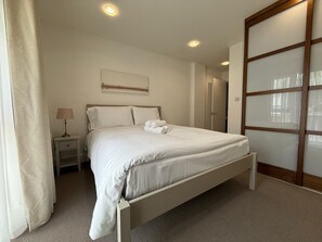 A bedroom with a bed, nightstands, a lamp, a painting, and a sliding door. - Westminster Apartment - Big Ben (London)
