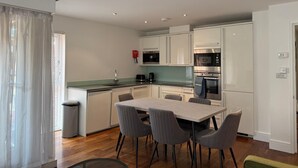 A modern kitchen with white cabinets, a dining table with chairs, and a trash bin. - Westminster Apartment - Big Ben (London)