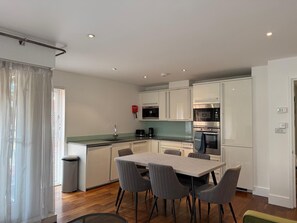 A modern kitchen with white cabinets, a dining table with chairs, and a trash bin. - Westminster Apartment - Big Ben (London)