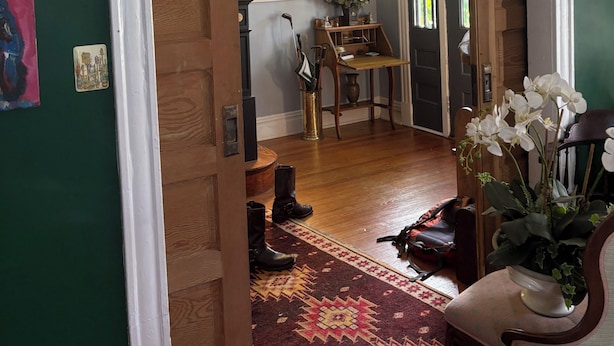 A room with a wooden floor, a patterned rug, a chair, a vase with flowers, and a wooden door. - Historic home in downtown Richmond by the James River (Richmond)