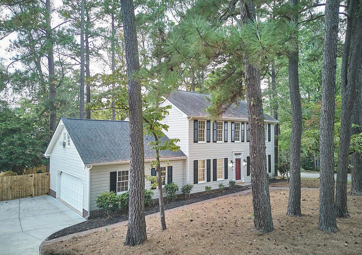 A two-story house with a garage, surrounded by tall pine trees.