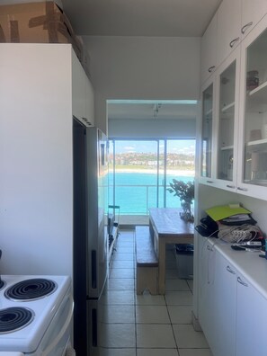 Una cocina estrecha con vista al mar, una zona de comedor y un refrigerador blanco.