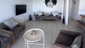A living room with a sofa, a coffee table, a TV, and a wall-mounted artwork.
