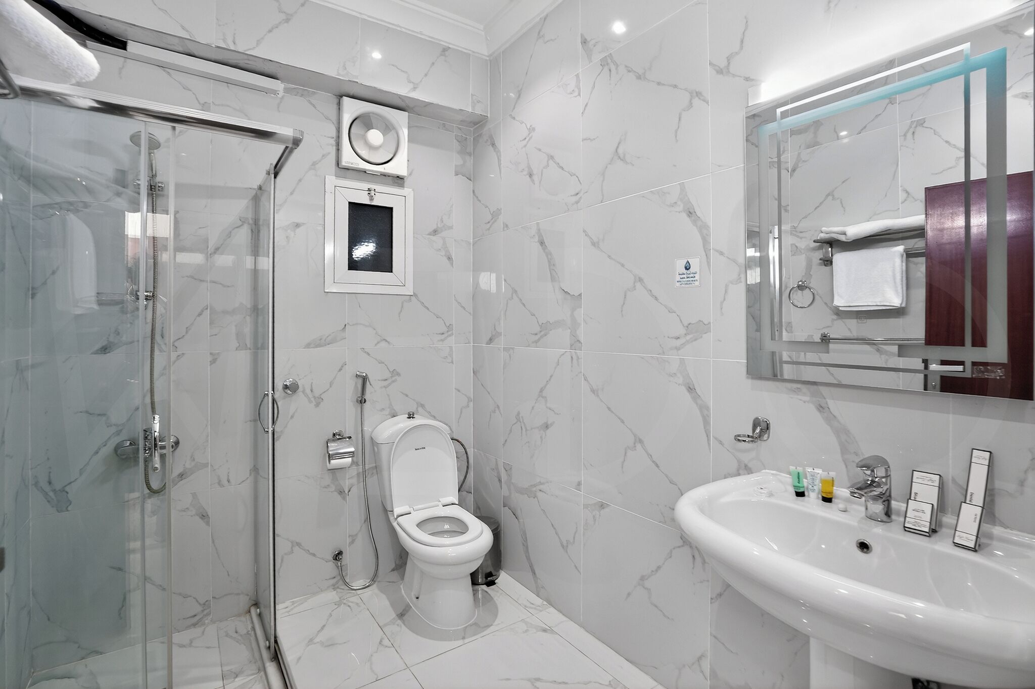 A modern bathroom with a glass-enclosed shower, a toilet, and a sink with toiletries.