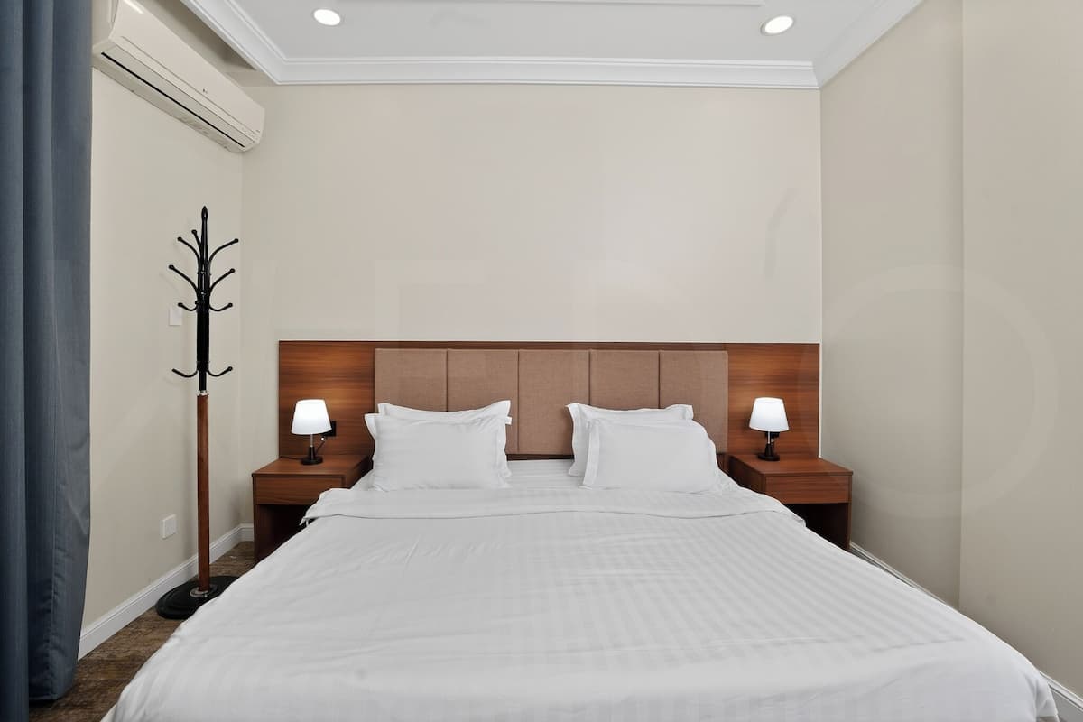 Ein Hotelzimmer mit einem großen Bett, zwei Nachttischen mit Lampen, einem Kleiderständer und einer Deckenleuchte.