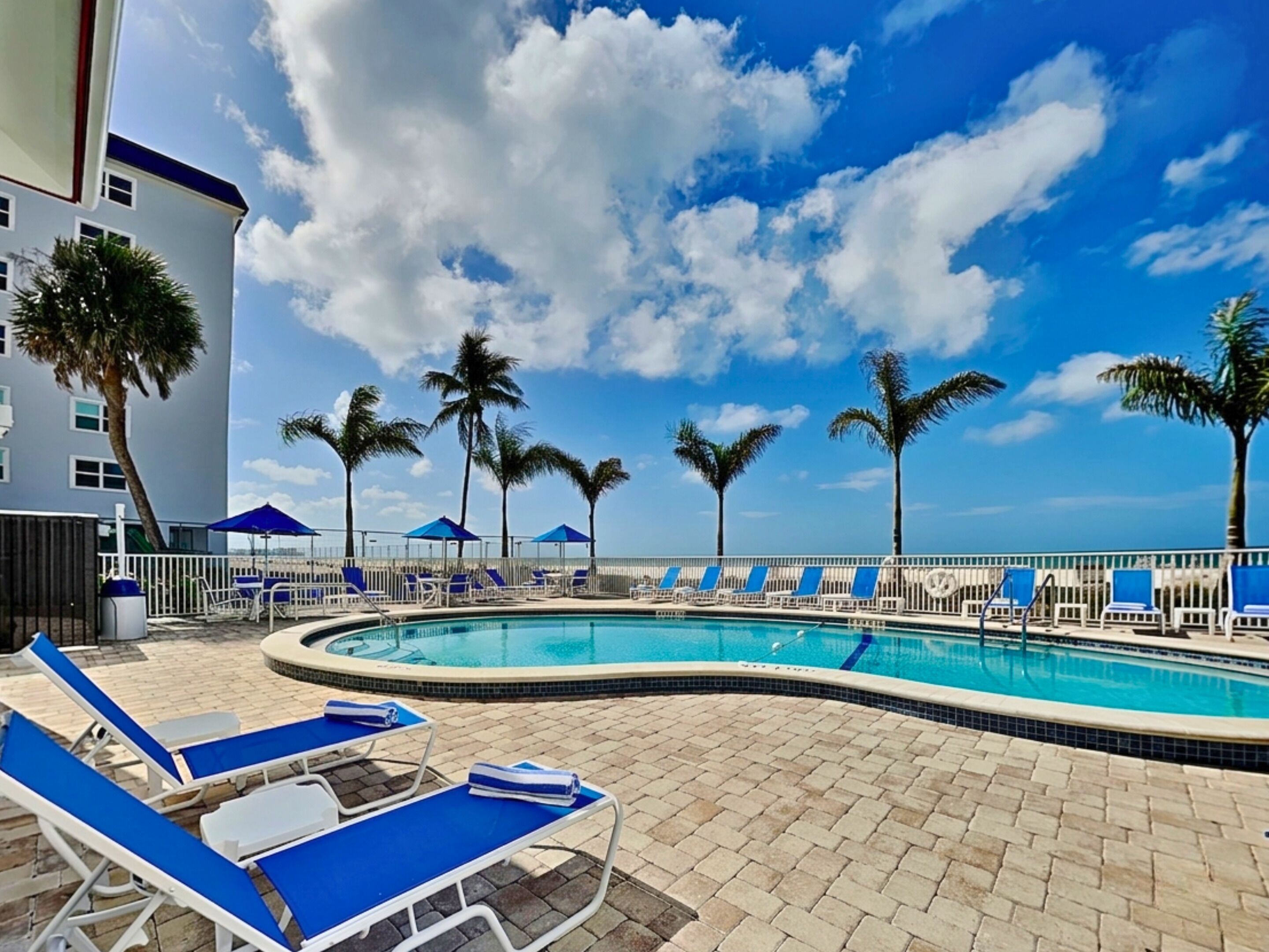 A pool area with lounge chairs, palm trees, and a clear sky.