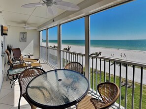 A balcony with a view of the beach, wicker furniture, and a ceiling fan. - Pointe South 304 | Gulf Front + Heated Pool (Fort Myers Beach)