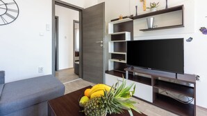 A modern living room with a flat-screen TV, a coffee table with fruits, a grey sofa, and a wooden door. - Vacation apartment close to the beach with private parking and barbecue (Novi Vinodolski)