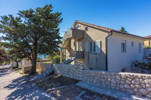 Une maison à deux étages avec un mur en pierre, un arbre et un ciel bleu dégagé.