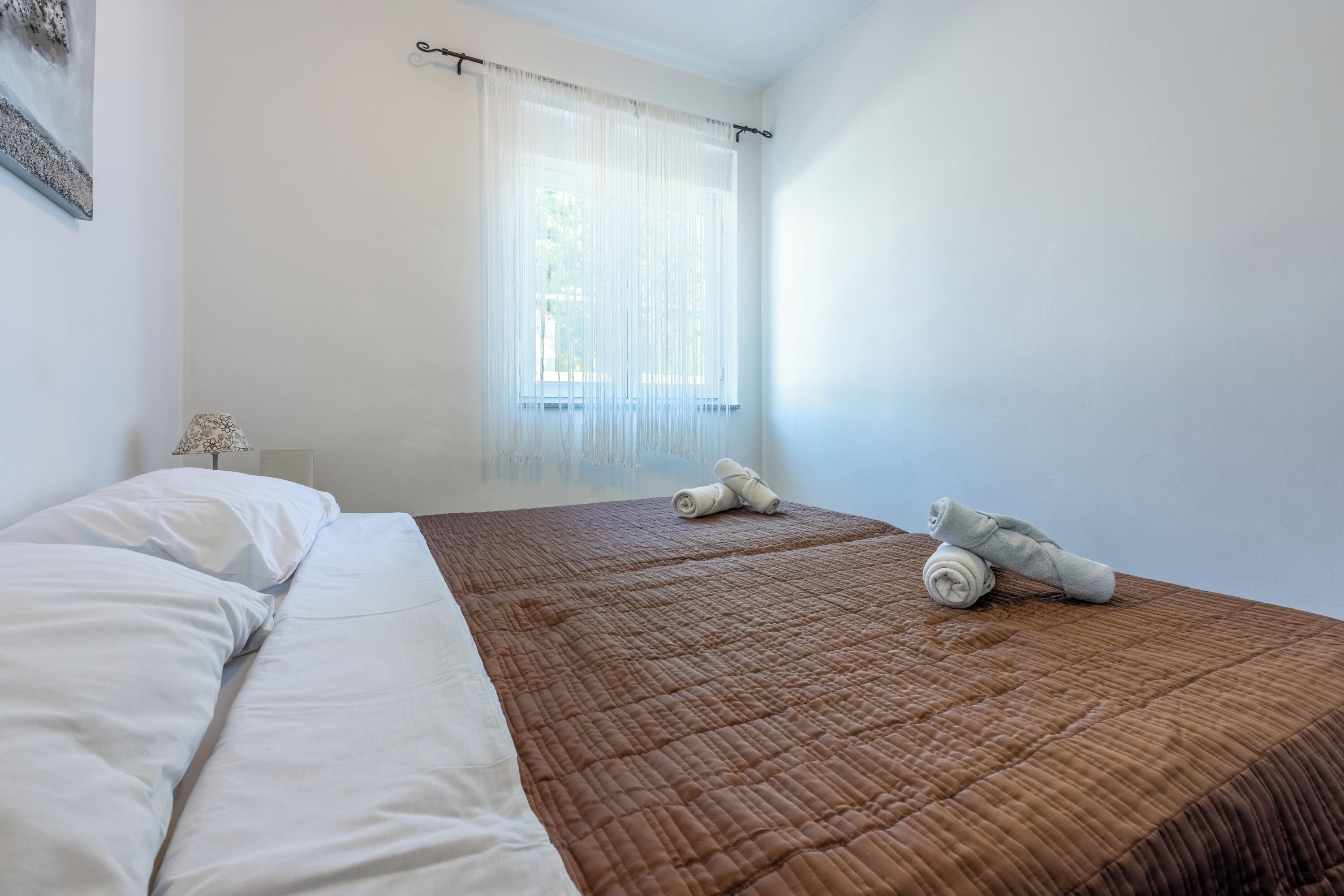Une chambre à coucher avec un lit, une fenêtre ornée de rideaux légers et un ours en peluche posé sur le lit.