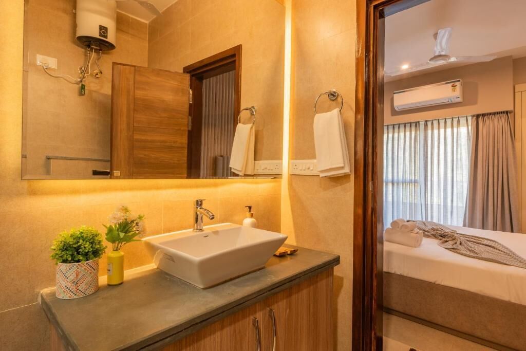 A hotel bathroom with a sink, mirror, towel rack, and an air conditioning unit.