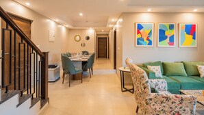 Una sala de estar moderna con un sofá verde, un sillón floral y una zona de comedor con mesa y sillas.
