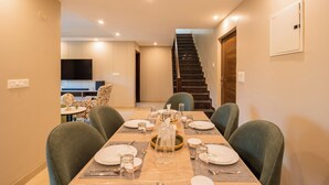 Un comedor con una mesa dispuesta para cuatro, sillas, un televisor al fondo y una escalera que lleva a otro nivel.