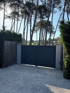 A gated driveway with a gravel surface, surrounded by tall trees and a wooden fence. - A 3-star-rated chalet-style house in a quiet location with a jacuzzi (optional)  (Le Teich)