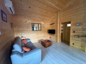 L’intérieur d’un chalet en bois, avec un canapé, un téléviseur et un miroir au mur.