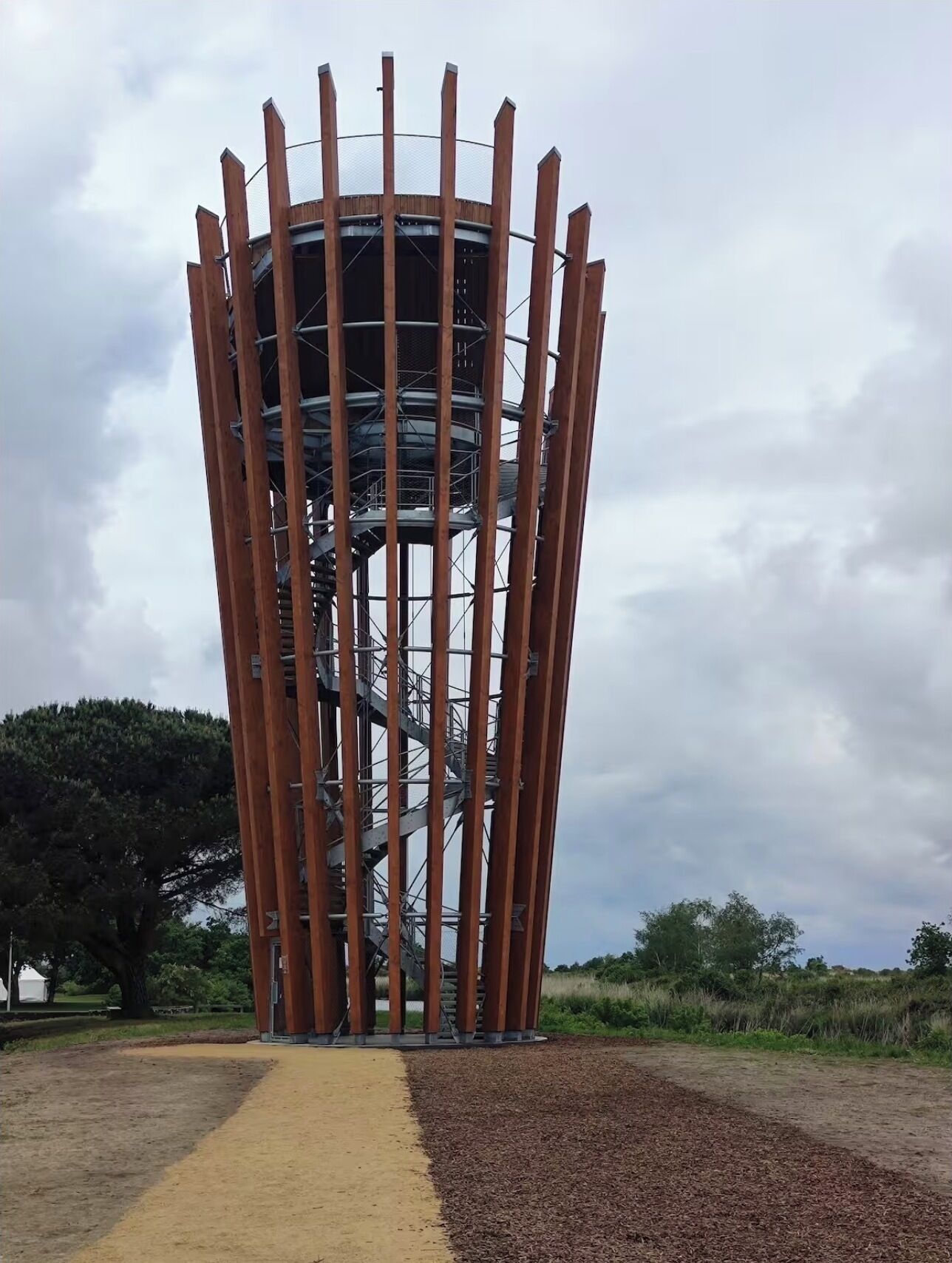 Una torre alta y cilíndrica con escalera en espiral, rodeada por una zona pavimentada con un sendero amarillo.