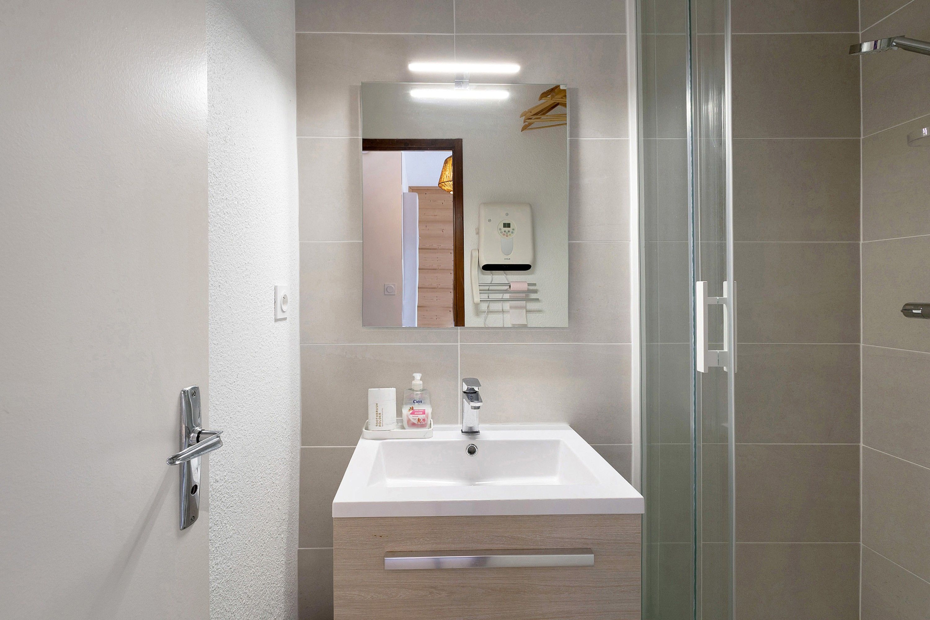 Un baño moderno con lavamanos blanco, espejo y cabina de ducha con paredes de vidrio.