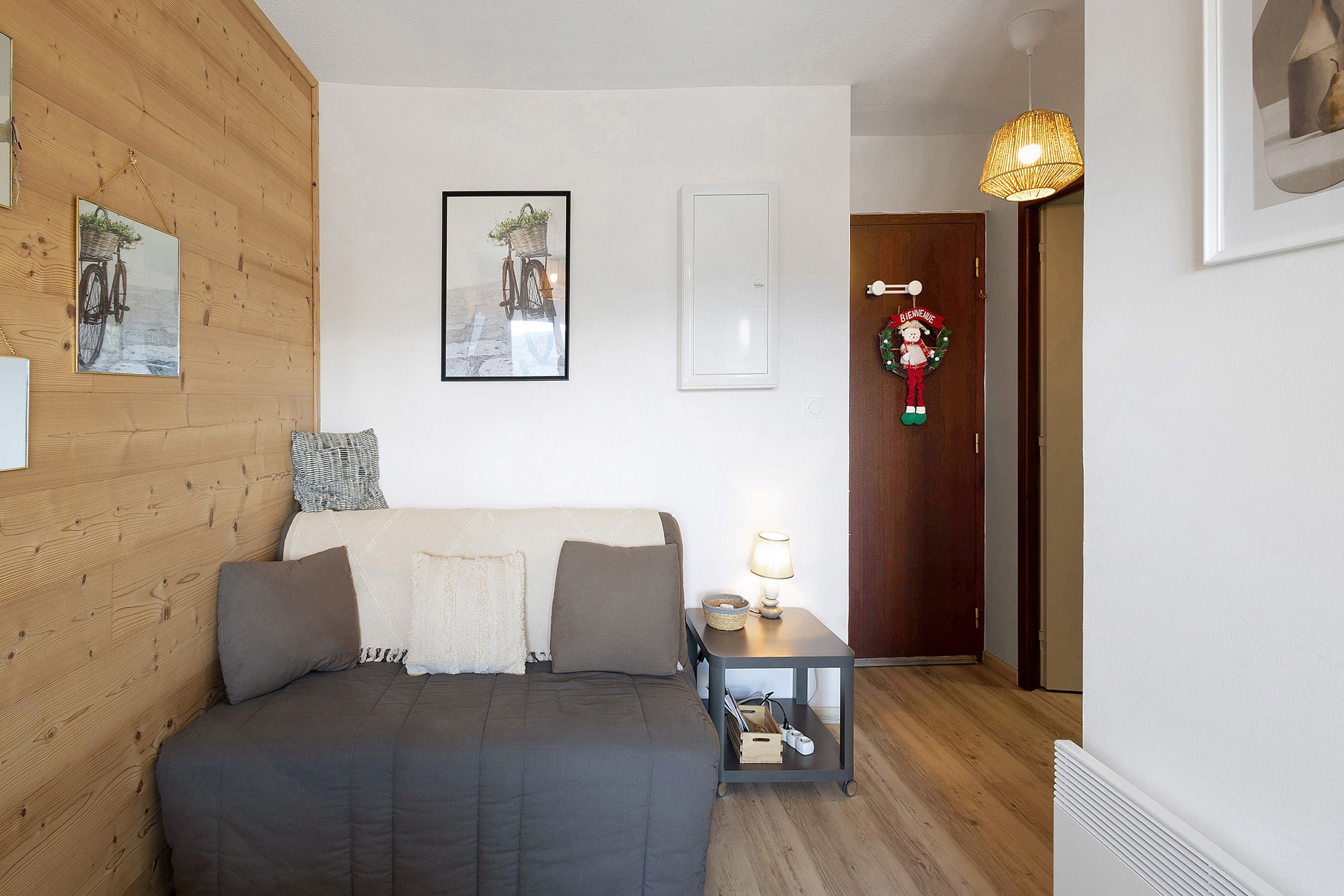 Un dormitorio con cama, mesita de noche, lámpara, puerta con letrero de bienvenida y un cuadro en la pared.