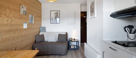 Una habitación pequeña con una pared de madera, una cama, una mesita, una kitchenette y un colgante de luz.