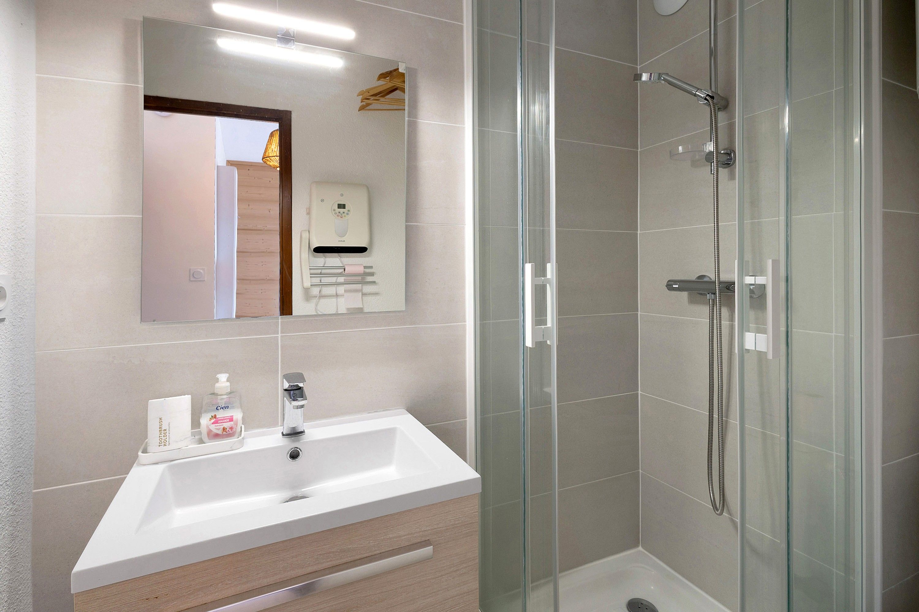 Un baño moderno con ducha envuelta en vidrio, un lavabo blanco y un espejo sobre él.