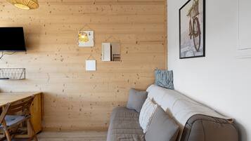 Una sala de estar moderna con una pared de madera, un televisor de pantalla plana, una zona de comedor con mesa y sillas de madera, y un sofá con cojines.