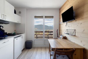 Una cuina compacta amb zona de menjador, un televisor fixat a una paret de fusta i vistes cap a l'exterior.