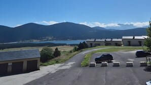 Un estacionamiento con un edificio a la izquierda, una carretera que se curva hacia la derecha y montañas al fondo.