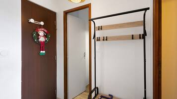 Una habitación con puerta de madera, lámpara fijada a la pared y literas de metal con estructura de madera.